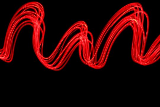 Long exposure photograph of neon red colour in an abstract swirl, parallel lines pattern against a black background. Light painting photography.
