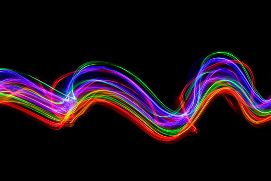 Long exposure photograph of neon colour in an abstract swirl, parallel lines pattern against a black background. Light painting photography.