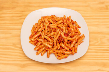 Simple and delicious plate of macaroni with chorizo on white plate and light wooden table