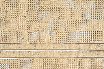 Texture of a wall of the facade of a building with multiple lines and holes painted in cream color