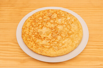 Great Spanish omelette with eggs and potatoes cooked in a pan on a light pine wood table