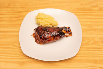 Charcoal-roasted pork knuckle with sauce and homemade mashed potatoes on a white plate and light pine wood table