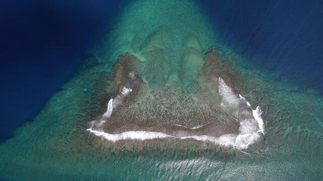 Scenic aerial view of a drone flying over a calm ocean with a coral reef to a tropical paradise island. Amazing nature landscape with blue lagoon and Pacific Ocean.