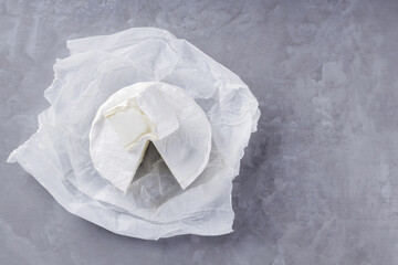 Camembert on a gray cement background. Soft cheese with white mold on parchment paper. Copy space. Top view
