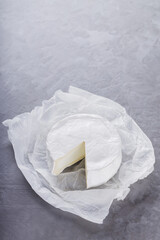 Camembert on a gray cement background. Soft cheese with white mold on parchment paper. Copy space. Top view