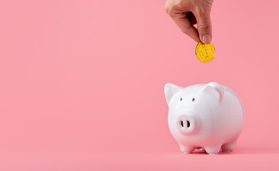 Money saving and investment concept. Hand putting Bitcoin coin to piggy bank on pink background with copy space