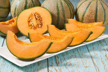 Sliced ripe sweet melon in a ceramic plate on a wooden table.