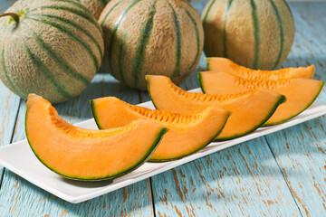 Sliced ripe sweet melon in a ceramic plate on a wooden table.
