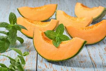 Sliced ripe cantaloupe melon and fresh mint on a wooden table.