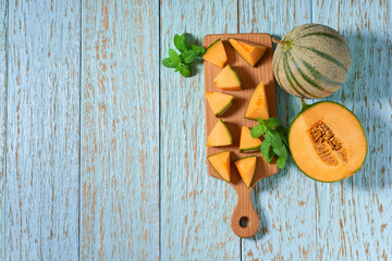 Sliced ripe cantaloupe melon and fresh mint on a wooden table, top view.