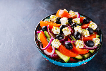 Greek salad in a bowl on a dark background. Healthy salad with feta cheese and olives. Fresh vegetable salad of Mediterranean cuisine. Copy space. Top view