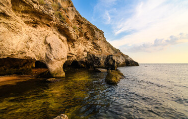 Seascape at sunset. Rocky coast with caves from sea waves.