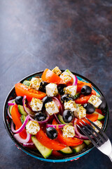 Greek salad in a bowl on a dark background. Healthy salad with feta cheese and olives. Fresh vegetable salad of Mediterranean cuisine. Copy space. Top view