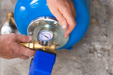 Blue metal tank of a pumping station with a pressure gauge. Installation of a water supply system in a residential building using a hydraulic accumulator