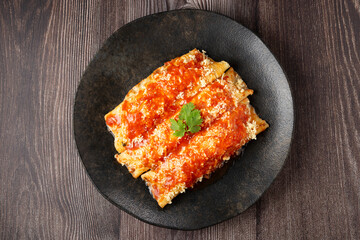 Pancakes stuffed with minced meat and topped with tomato sauce and grated cheese.