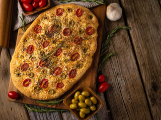Traditional fragrant Italian bread - focaccia, olives, tomatoes, sprigs of rosemary, garlic on a...