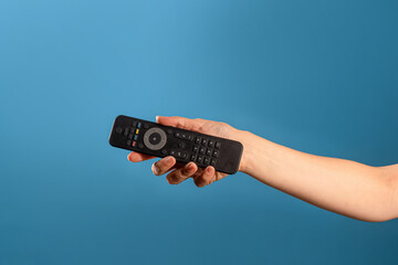Watch new TV series and movies at home on streaming services, the TV remote control is in a female hand, switch channels. Photo on a blue background