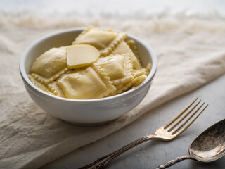 On the white tablecloth is a serving bowl of Italian ravioli. Next to it are a fork and a spoon. Close-up. Restaurant, hotel, cafe, home cooking, cooking blog, cookbook.
