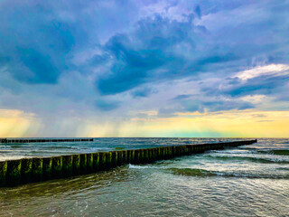 Obraz premium blue and yellow thunderclouds over a beach with green water and Groynes in a thunderstorm hurricane with lots of waves.