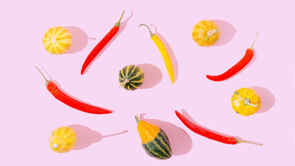 pattern made of yellow and red hot chili peppers and yellow and green pumpkin on pastel pink background. Happy and healthy autumn food creative concept. Red, pink and yellow colorful artistic design.