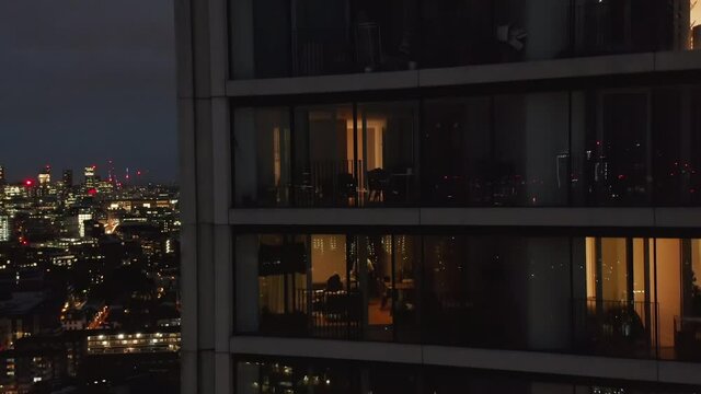 Luxury apartment in modern tall residential building at night. Close up view of into windows. Crane up shot. London, UK