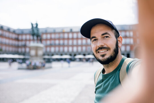 Young backpacker tourist taking selfie photo with smartphone outdoors - Happy man visiting Plaza Mayor in Madrid, Spain - Tourism and vacation concept