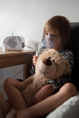 Przeziębiony chłopiec siedzący przy stole z inhalatorem i pluszowym misiem - obrazy, fototapety, plakaty