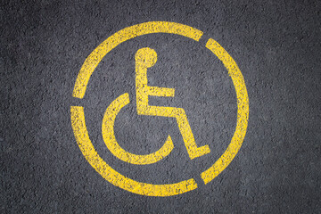 Top view of yellow wheelchair sign painted on the asphalt road marking a parking lot for disabled or handicapped persons.
