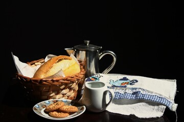Breakfast with fresh bread, biscotiso, teapot and cup of black coffee in the sunlight