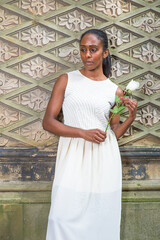 Dressing in white and holding a white rose,  a young pretty black girl is standing by an ancient...