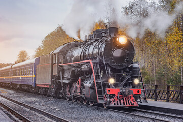 Fototapeta na wymiar Retro steam train departs from the station wooden platform.