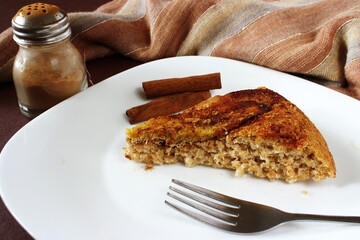 Piece of banana pie on white plate and fork cinnamon stick and powder on fabric