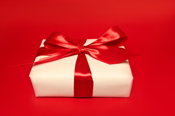A gift box with big red bow against red background. Holidays concept
