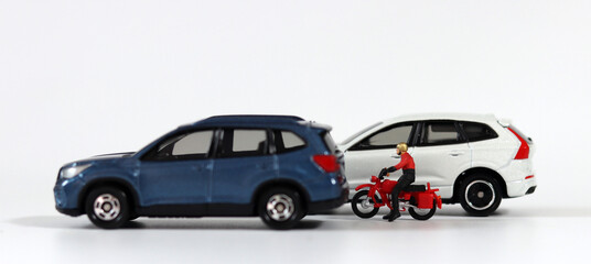 A motorcycle driver between a blue car and a white car. Miniature people and miniature cars.
