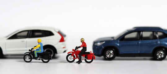 Miniature motorcycle messenger between miniature cars. Miniature people and miniature car. 
