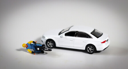 Miniature people and miniature car. A miniature motorcycle driver who fell in front of a white miniature car. Concept about a dangerous motorcycle accident.
