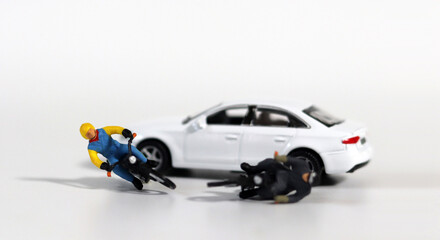 Miniature people and miniature car. White cars and fallen motorcycle drivers. Concept about the dangers of speeding motorcycles.
