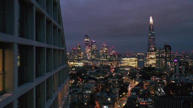Elevated forwards fly around modern tall apartment building. Revealing panoramic view of night cityscape. London, UK