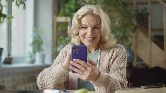  An old woman makes calls to her relatives via video communication. She pushes a button on the phone and waves her hand