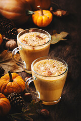 Pumpkin butter latte or coffee, keto drink on wooden table with fallen leaves, small pumpkins, pine cones and nuts. Autumn and winter hot drink and beverage