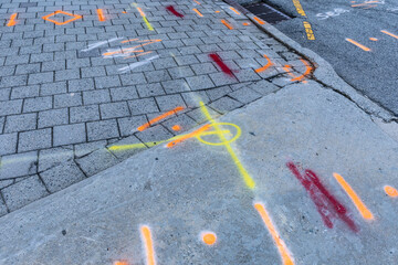 Yellow, orange, and red spray painted lines across a sidewalk of concrete and grey block,...