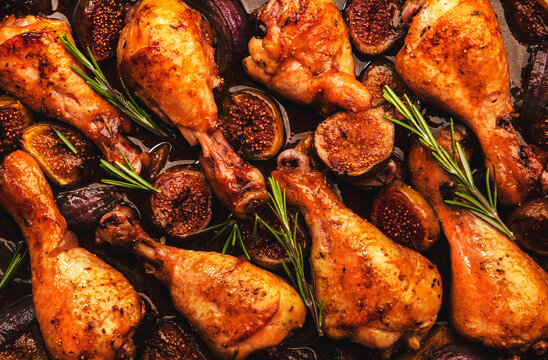 Baked chicken legs, drumsticks with sweet figs and red onions in balsamic marinade on baking sheet, close up, top view