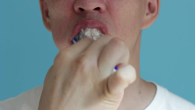 Man brushes his teeth with a toothbrush close-up on blue background.