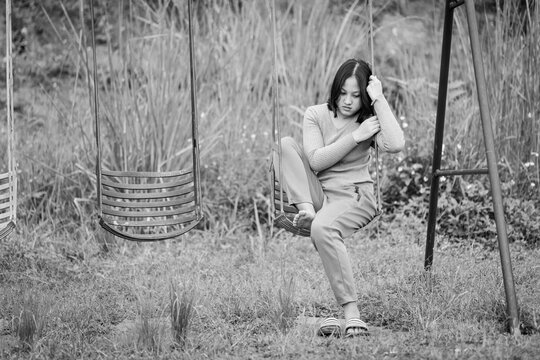 Sad and depressed young teenage girl sitting on swing in park. black and white image