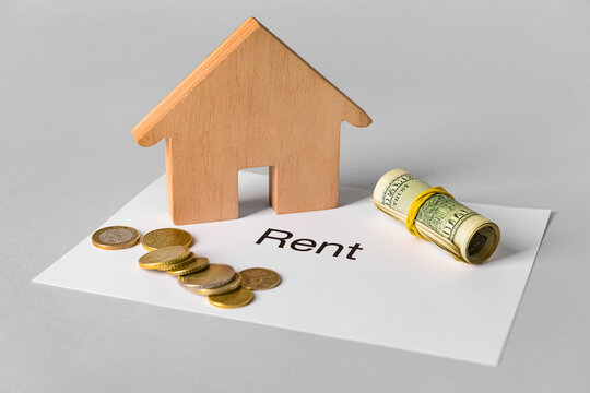 Wooden house with word RENT and money on light background