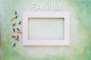 Top down perspective of the word FAMILY above a white picture frame on green painted canvas with Christmas Light decorations; Christmas card template of white empty picture frame and the word FAMILY