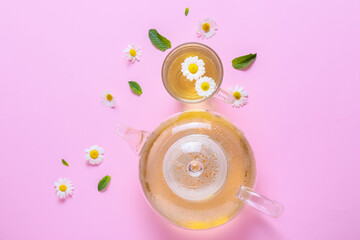 Teapot and cup of tasty chamomile tea with flowers on color background