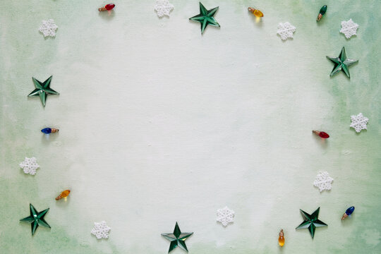 Top down perspective of a green painted canvas with a border of Christmas decorations; Stars, snowflakes and Christmas light decorations surround an empty space creating a frame