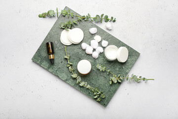 Board with cosmetic products, cotton pads, balls and eucalyptus branches on light background