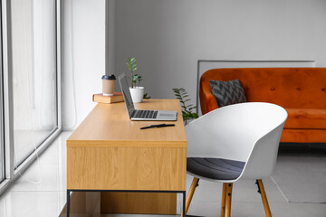 Wooden table with laptop near window in modern living room